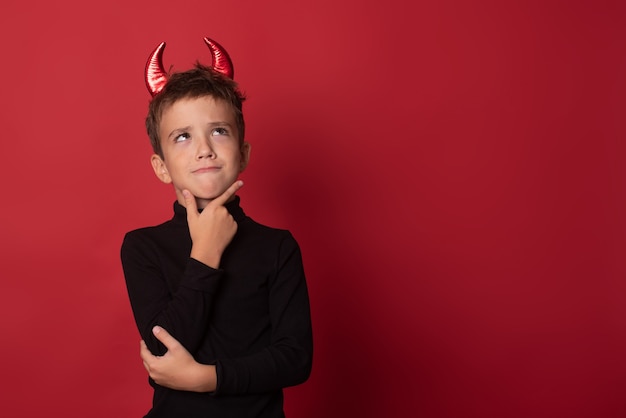 Halloween Glückliches Kind lacht laut mit teuflischen Hörnern vor einem roten Studiohintergrund