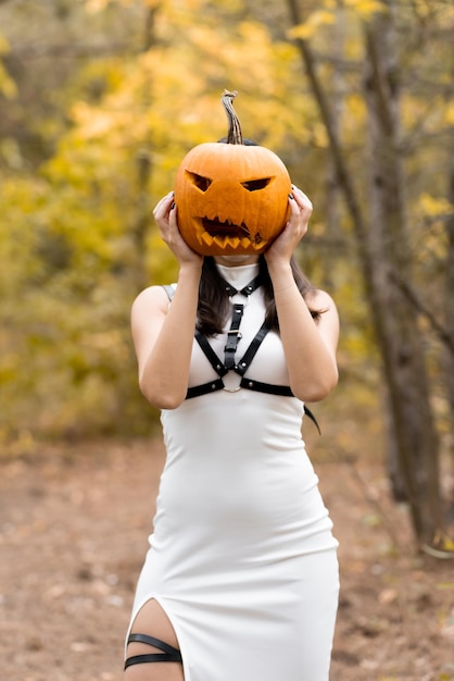 Halloween Hermosa joven con un vestido blanco posando en el bosque de otoño Sostiene una calabaza por cabeza El día de los muertos