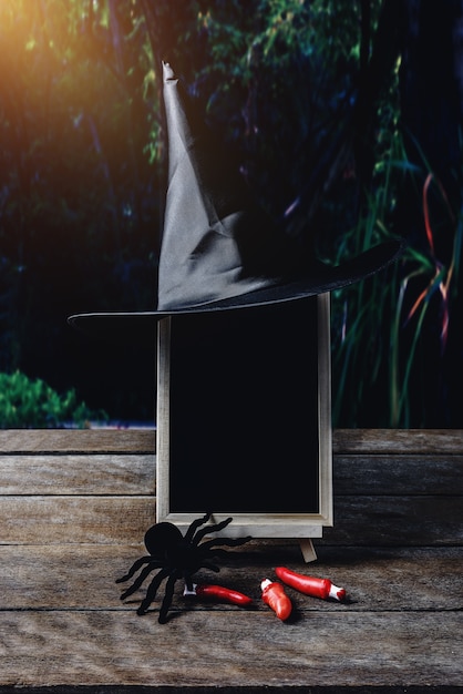 Halloween-Hintergrund. Hexenhut, schwarze Spinne, Tafel auf Bretterboden und dunkler Wald