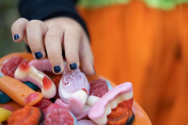 Halloween-Hintergrund. Kinderhände greifen nach der gruseligen Süßigkeit auf dem Teller