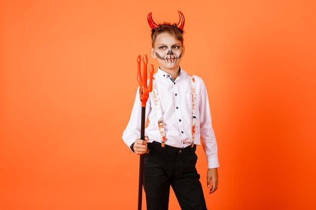 Halloween-Junge mit Teufelshörnern mit Heugabeln auf orange Wandhintergrund. Hochwertiges Foto