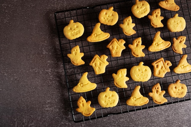 Halloween-Kekse in Form eines Kürbises, eines Hexenhutes, eines Geistes und eines schrecklichen Hauses auf einem schwarzen Rost zum Backen