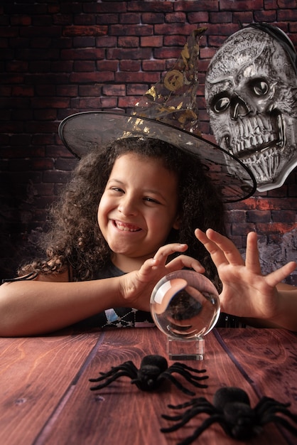 Halloween, kleines Mädchen, das in einer Halloween-Einstellung mit einer Kristallkugel spielt, selektiver Fokus.