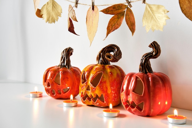 Halloween-Komposition mit keramischen Kürbissen, Jack-Laterne und Kerzen auf dem Hintergrund der Tischwand Heimdekoration