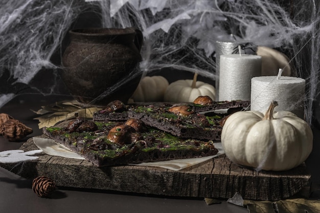 Halloween-Konzept Essen. Fladenbrot oder Pizza mit Tintenfischtinte, grünem Käse, Pilzen und lila Zwiebeln. Totenbrot mit festlichem Dekor, weißem Kürbis, Kerzen und Spinnennetz. Dunkler Steinhintergrund