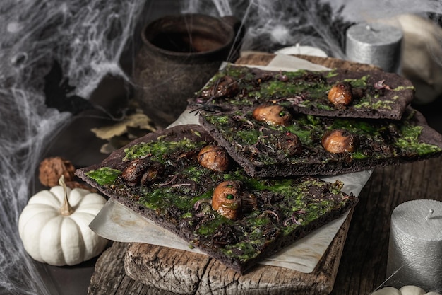 Halloween-Konzept Essen. Fladenbrot oder Pizza mit Tintenfischtinte, grünem Käse, Pilzen und lila Zwiebeln. Totenbrot mit festlichem Dekor, weißem Kürbis, Kerzen und Spinnennetz. Dunkler Steinhintergrund