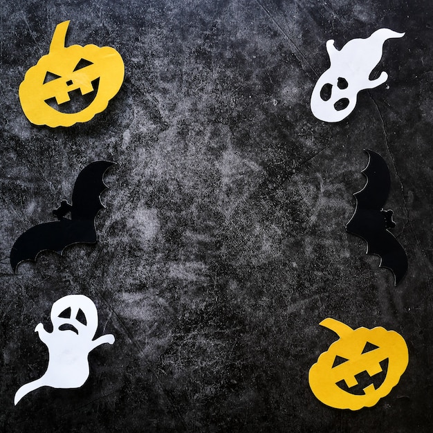 Halloween-Konzept mit Kürbisen, Geistern und Schlägern schnitt Papier auf schwarzem konkretem Hintergrund.
