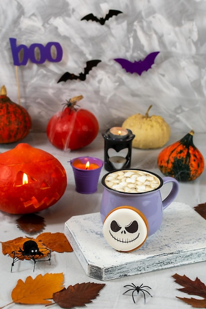 Halloween-Kürbis und Tasse Kaffee mit Keksen auf dem Hintergrund einer grauen Wand mit Geistern, Fledermäusen, Spinnen, Kerzen, Kürbisblättern, selektiver Fokus
