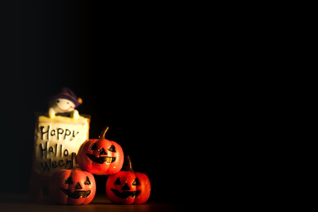 Halloween-Kürbisse mit bemalten Gesichtern und Geisterpuppen auf schwarzem Hintergrund des alten Holzschreibtischs und Kopienraum für Text