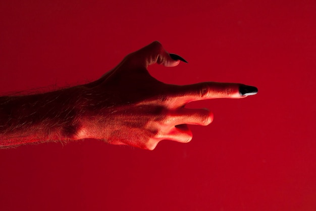 Halloween-Monsterhand des roten Teufels mit schwarzen Fingernägeln gegen einen roten Hintergrund