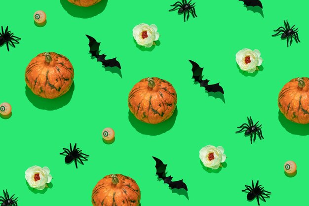 Halloween-Muster mit orangefarbenen Kürbissen, schwarzen Fledermäusen und Spinnenaugäpfeln und weißen Blumen auf grünem Hintergrund