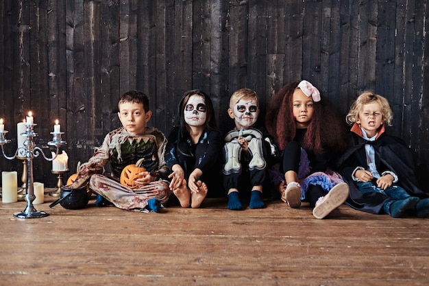 Halloween-Party mit Gruppenkindern, die zusammen auf einem Holzboden in einem alten Haus sitzen.