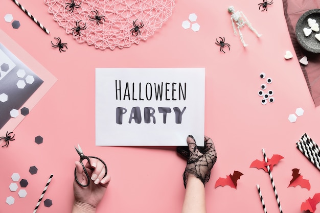 Halloween-Partytext auf weißer Seite in der Hand gehalten. Flache Lage mit schwarz-weißen Dekorationen, Hand halten Seite mit Text