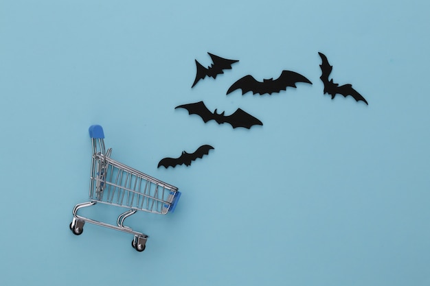 Halloween-Rabatte, Einkaufen. Supermarktlaufkatze und fliegende Schläger auf Blau Halloween Dekoration