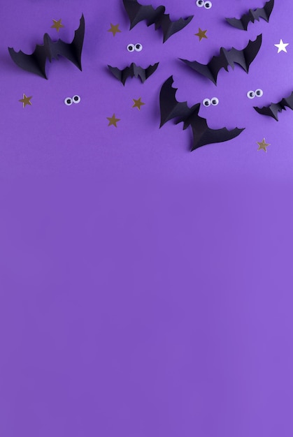 Halloween-Rahmenschablone mit schwarzen Papierfledermäusen und gruseligen Plastikaugen auf einem farbigen violetten Hintergrund.