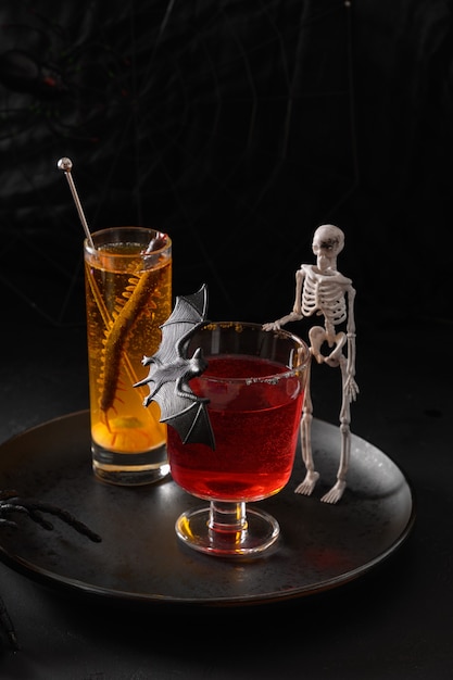 Halloween rote und orangefarbene alkoholische Cocktails verzierten Fledermaus und Skelett auf Schwarz
