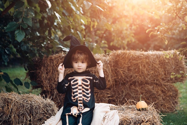 Halloween-Skelett-Kind-Junge, der auf dem Heuhaufen sitzt glücklicher Tag kleines Kind genießt den Spaziergang glücklich lachend ...