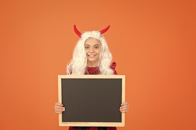 Halloween-Teufelskind in Koboldhörnern halten Schultafel für Kopienraum glückliches Halloween