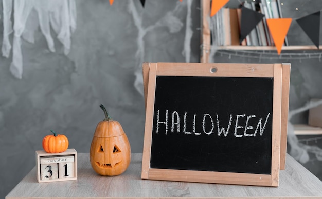 Halloween-Text auf schwarzem Tafelholztisch mit Kalender vom 31. Oktober und orangefarbenem Kürbis. Konzept einer fröhlichen Halloween-Feiertagsatmosphäre zu Hause