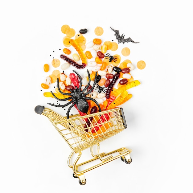 Halloween trata em um carrinho de compras em um fundo branco. doçura ou travessura, conceito para o halloween. camada plana, vista superior