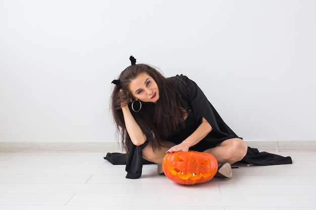 Halloween- und Maskerade-Konzept - Schöne junge Frau, die mit Kürbis-Kürbislaterne aufwirft
