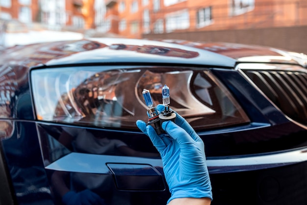 Halogenlampe in der Hand eines Mannes vor dem Hintergrund der Scheinwerfer eines schönen Autos