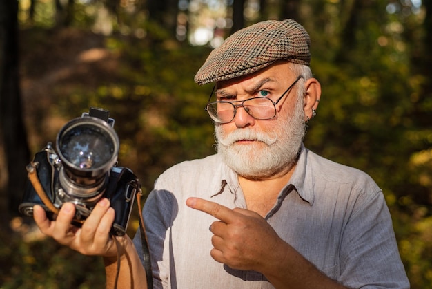 Halten Sie an oder fotografieren Sie. Alter Kameramann zeigt mit dem Finger im Sommer im Freien. Fotoshooting-Sitzung. Reise-Shooting. Mieten Sie einen Urlaubsfotografen