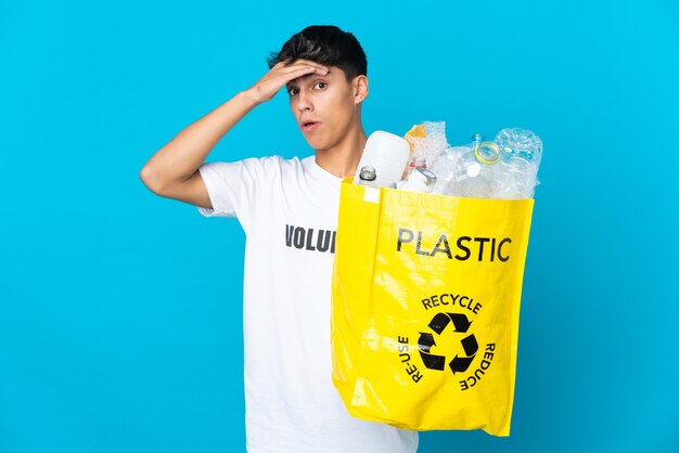 Halten Sie eine Tasche voller Plastikflaschen, um sie über die blaue Wand zu recyceln, und machen Sie eine Überraschungsgeste, während Sie zur Seite schauen