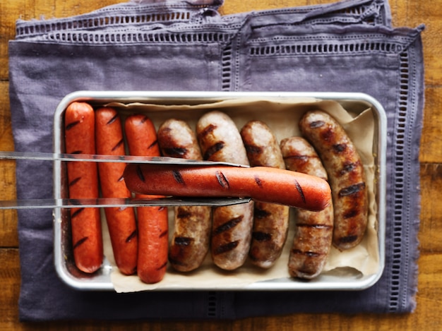 Halten Sie gegrillten Hotdog mit einer Zange über ein Tablett mit gegrilltem Fleisch