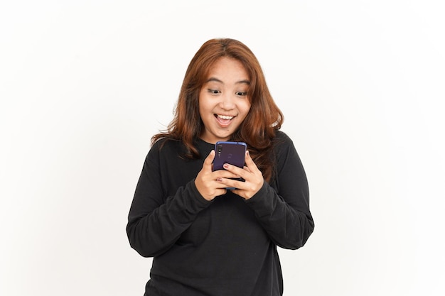Halten und Verwenden des Smartphones einer schönen asiatischen Frau, die ein schwarzes Hemd, isoliert auf weiss, trägt