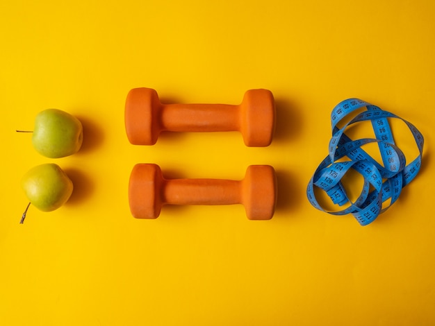 Halteres para fitness, maçãs e fita métrica sobre um fundo amarelo. conceito de perda de peso. flatlay, copyspace.