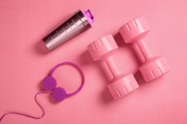 Halteres rosa, fones de ouvido e shaker de proteína no tapete de fitness