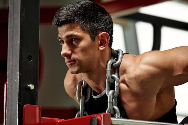 Halterofilista com uma enorme corrente de metal em volta do pescoço flexões nas barras irregulares da academia