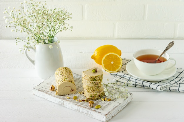 Halva com pistache servido na mesa de madeira branca com flores e chá.