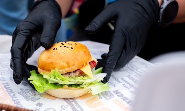 Foto hamburger mini profissional chef de mão segurando fresco delicioso e saboroso hambúrguer feito à mão adornado com salada de tomates e pepino em uma foto em close-up comida rápida para o seu estilo de vida rápido