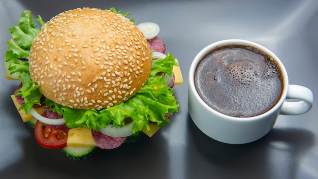 Hamburger mit gemüse und wurst und kaffee auf grauem hintergrund. fast food und frühstück. kalorien und ernährung.