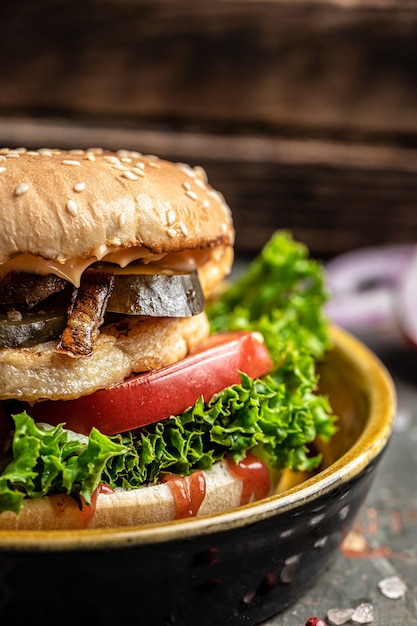 Hamburger mit Hühnchen, Essiggurken und Röstzwiebeln. Rindfleischburger auf hölzernem Hintergrund. vertikales Bild. Platz für Text