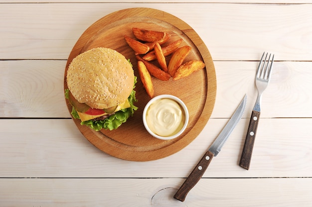 Hamburger mit Idaho-Kartoffeln und Käsesoße auf einem runden hölzernen Brett