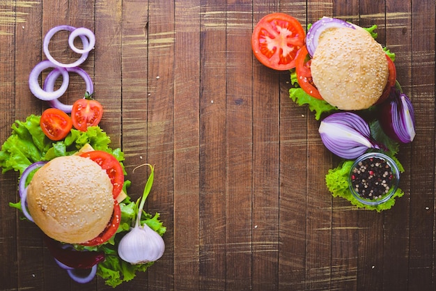 Hamburger mit Käsefleischtomaten und -zwiebeln und -kräutern auf Draufsicht des hölzernen Hintergrundes Freier Platz