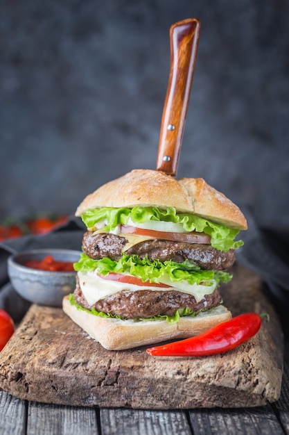 Hamburger mit Rindfleischburger und frischem Gemüse auf dunklem Hintergrund. Leckeres Fastfood.