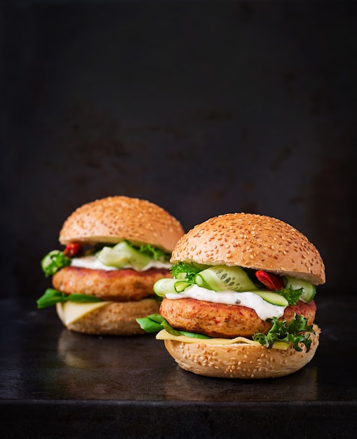 Hamburger mit saftigem Chicken Burger, Käse, Gurke, Chili und Tartarsauce auf schwarzem Tisch