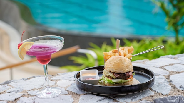 Hamburger und ein Cocktail beim Mittagessen in einem Restaurant mit Blick auf das Schwimmbad