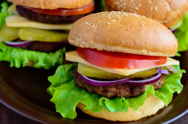 Hamburger zu Hause (Brötchen, Tomate, Gurke, Zwiebelringe, Salat, Schweinekoteletts, Käse) in einer Tonschale auf einem hölzernen Hintergrund. Nahansicht