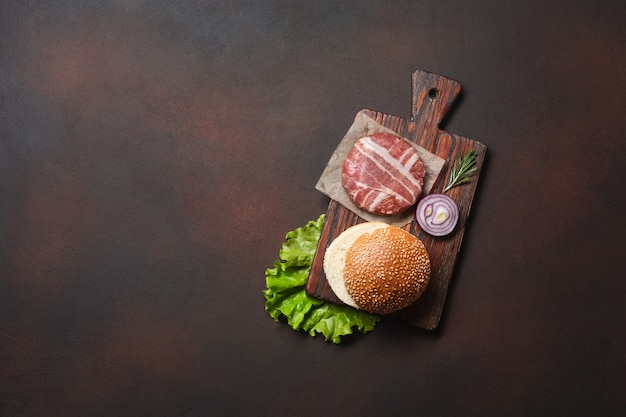 Hamburger Zutaten rohes Schnitzel, Salat, Brötchen, Gurken und Zwiebeln auf rostigem Hintergrund. Draufsicht mit Platz für Ihren Text.