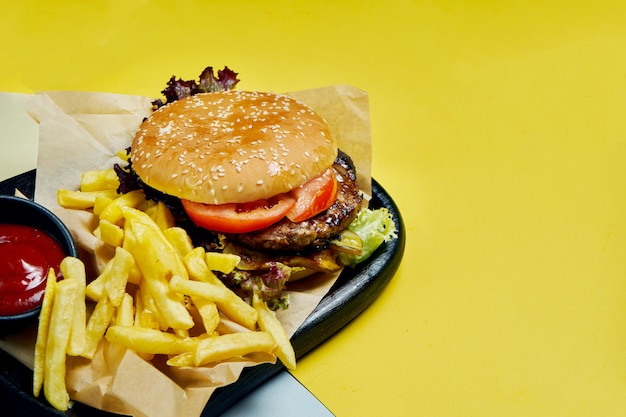 Hambúrguer americano apetitoso com carne, tomate, alface e batata frita em uma bandeja preta sobre uma superfície colorida Fast-food saboroso