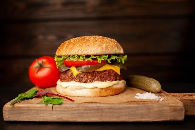 Hambúrguer caseiro com alface, tomate, queijo e pepino em uma placa de corte