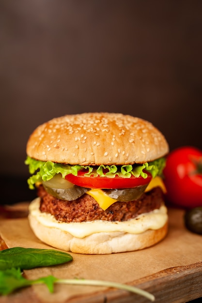 Hambúrguer caseiro com alface, tomate, queijo e pepino em uma placa de corte