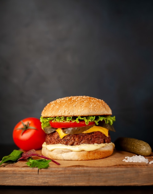 Hambúrguer caseiro com alface, tomate, queijo e pepino em uma placa de corte