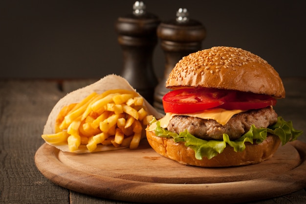 Hambúrguer caseiro com carne, cebola, tomate, alface e queijo. Hambúrguer fresco fechar na mesa rústica de madeira com batata frita, cerveja e batatas fritas. Hamburguer de queijo.