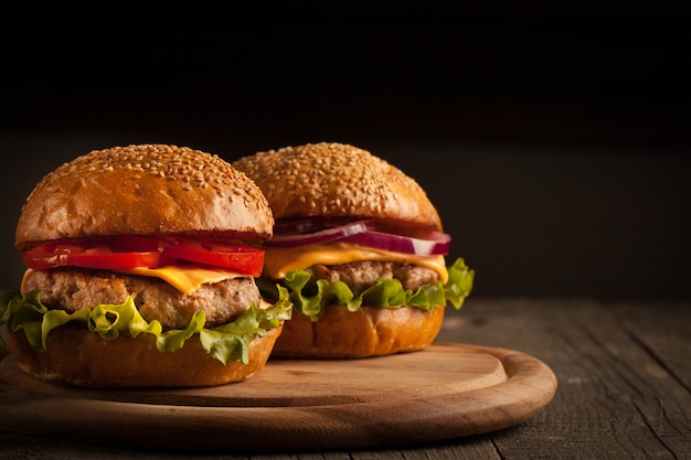 Hambúrguer caseiro com carne, cebola, tomate, alface e queijo. hambúrguer fresco fechar na mesa rústica de madeira com batata frita, cerveja e batatas fritas. hamburguer de queijo.